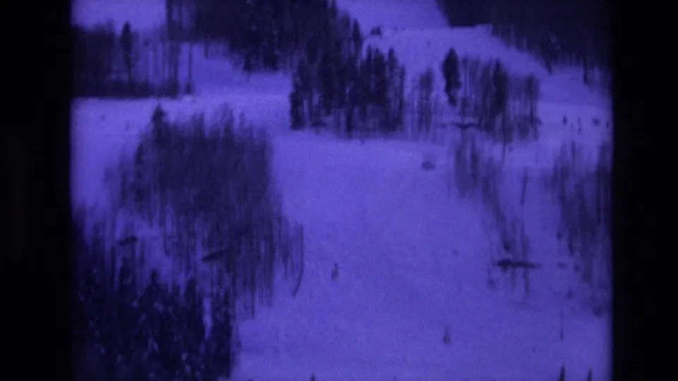1974 Vail, Colorado home-movie frame showing a snowy hillside with scattered trees, faint ski tracks, and distant lift structures under a purple film tint.