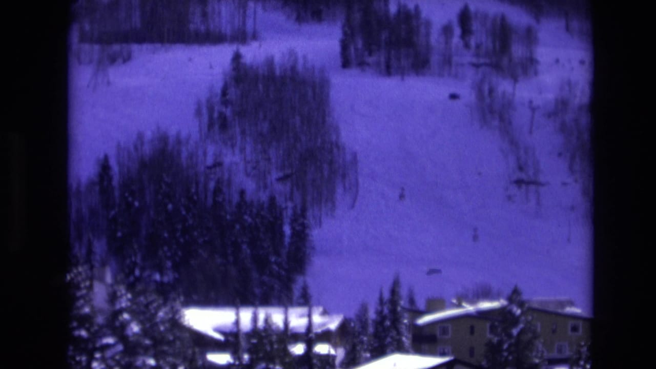 1974 Vail, Colorado view of a snow-covered ski hillside with small distant figures, evergreen trees, and resort buildings along the lower edge of frame.