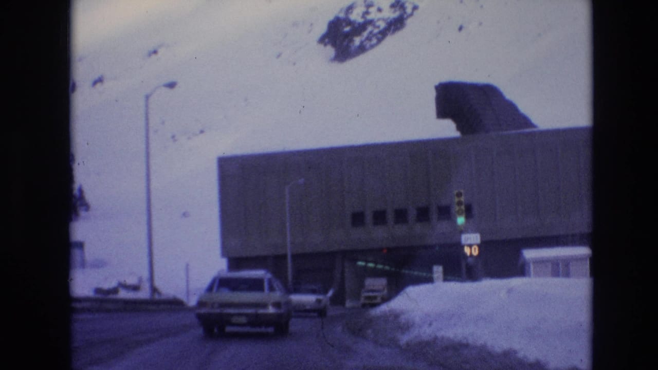 Car nears a concrete tunnel entrance beside snowbanks and a traffic signal.
