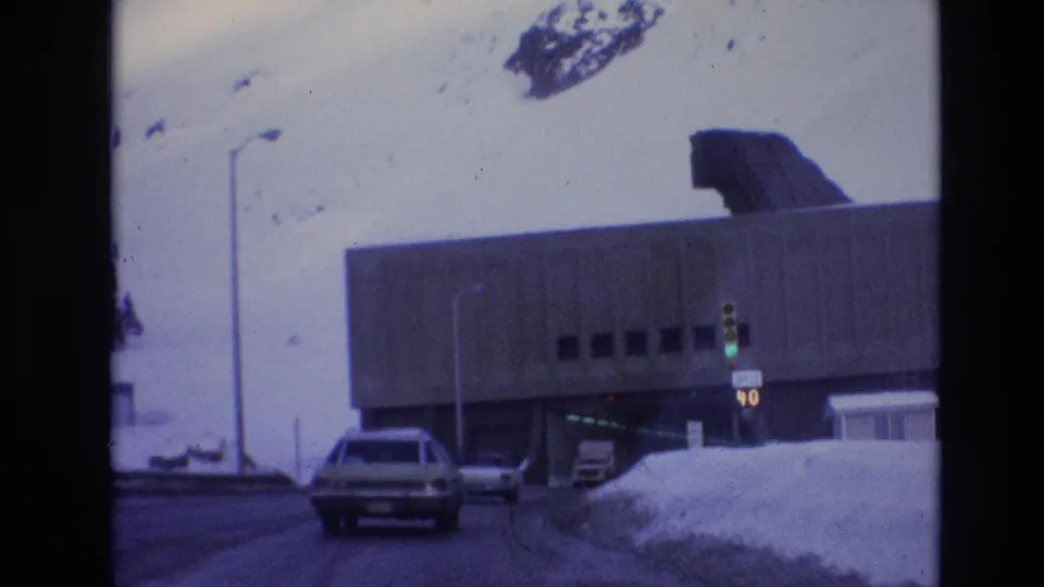 1974 Vail, Colorado frame with a car approaching a concrete tunnel-like entrance, a green traffic light, roadside snowbanks, and a speed limit 40 sign.