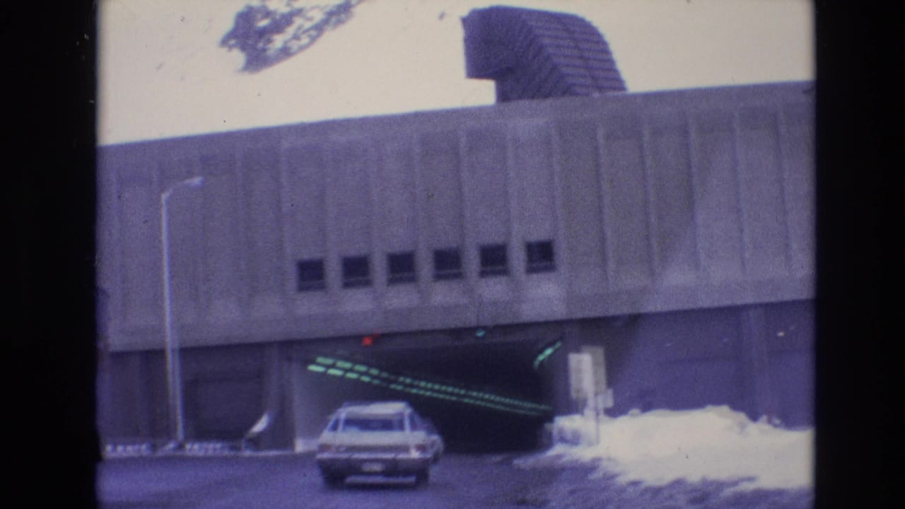 A 1974 Vail, Colorado road scene shows a white station wagon nearing a concrete tunnel entrance with snow piled along the roadside.