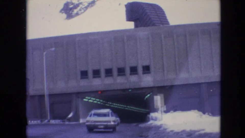 A 1974 Vail, Colorado road scene shows a white station wagon nearing a concrete tunnel entrance with snow piled along the roadside.