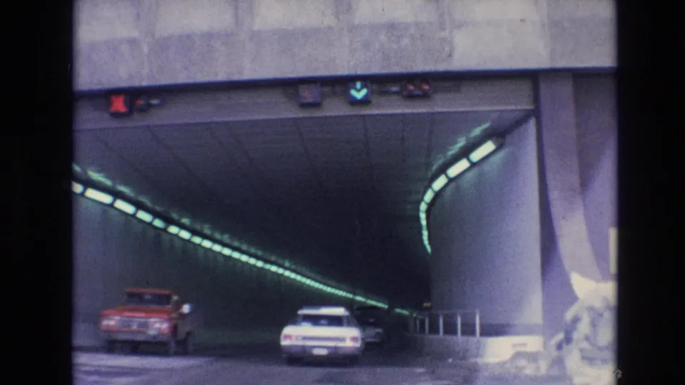 Two cars travel into the green-lit tunnel interior in the supplied 1974 Vail, Colorado footage, with the concrete portal and snowy roadside still visible at frame edge.