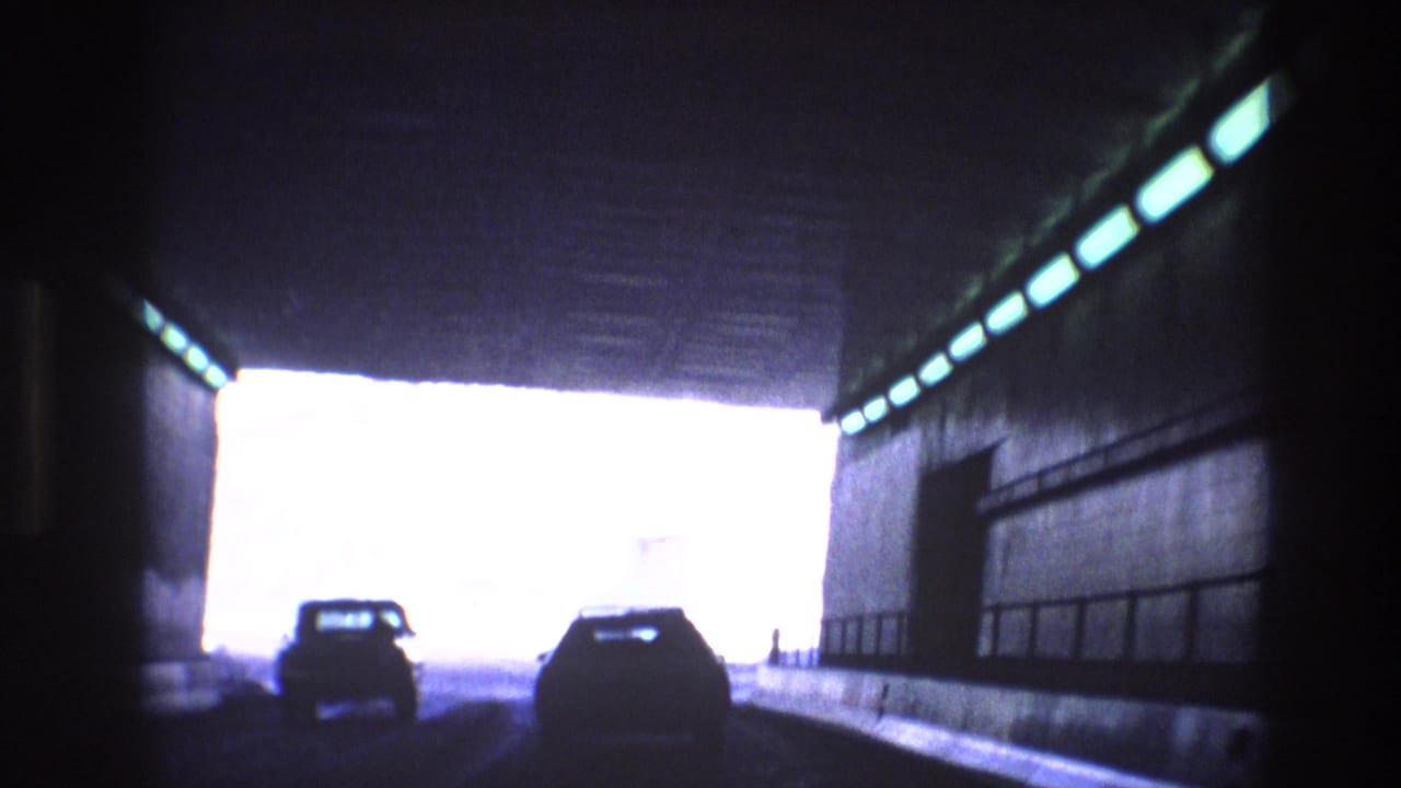 Cars approach a bright tunnel exit from inside a dark roadway tunnel.