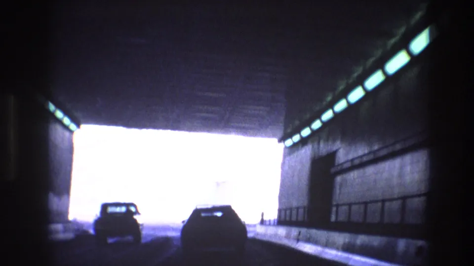 Cars are silhouetted as they drive toward the bright exit of a highway tunnel in the Vail, Colorado road-trip footage.