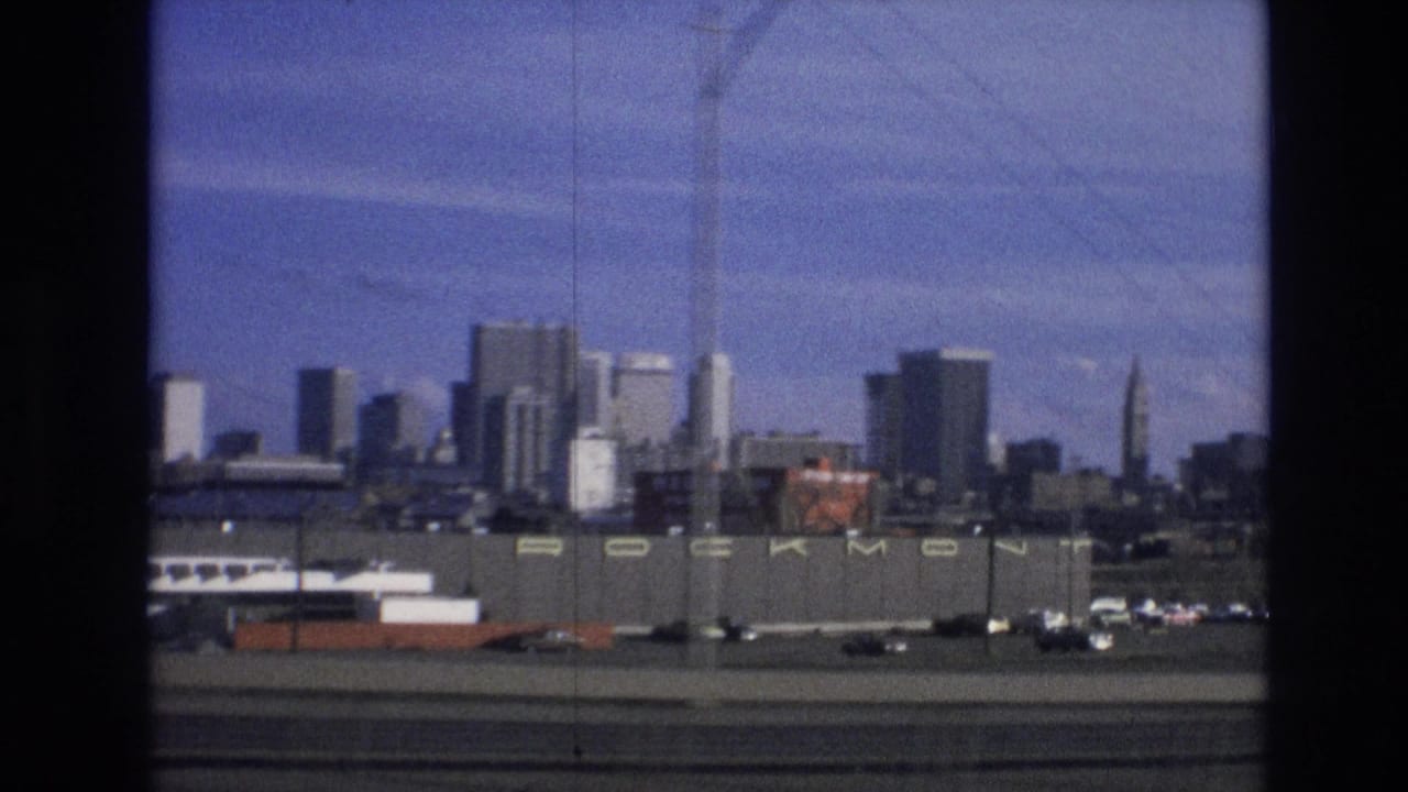 Distant city skyline behind an industrial foreground and roadway, seen through dark frame borders.