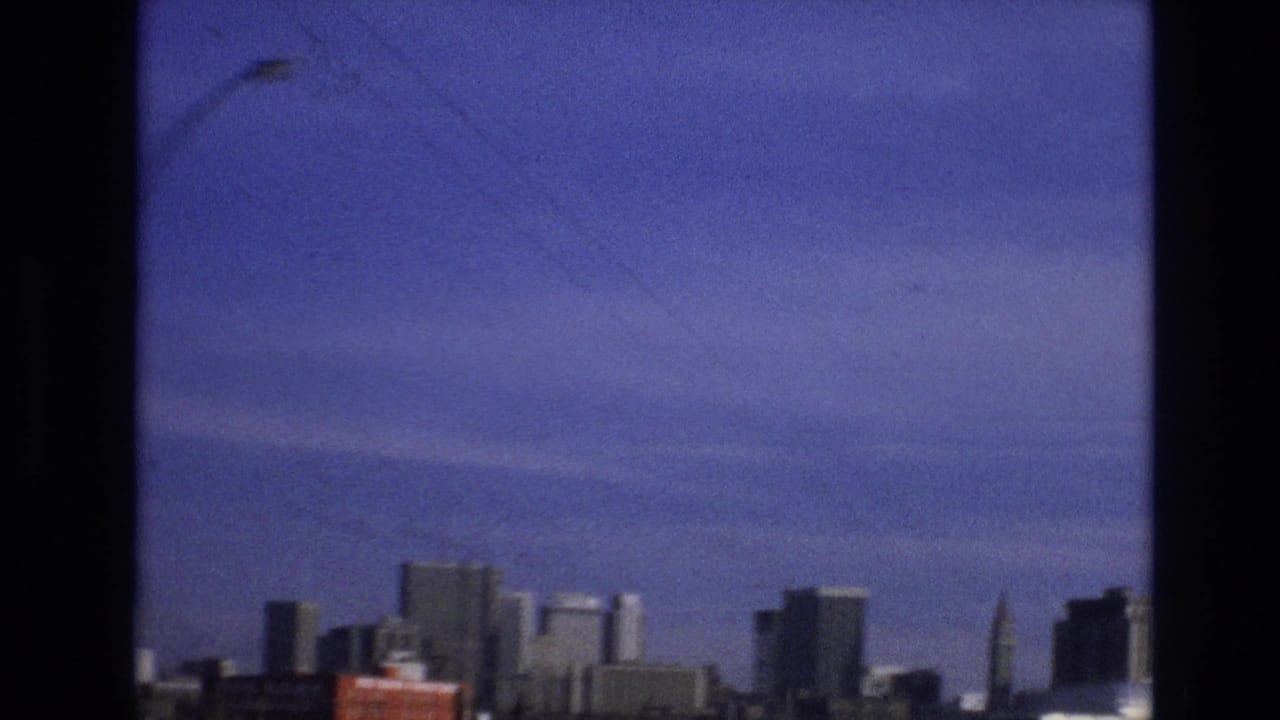 1974 8mm frame identified as Vail, Colorado, showing a distant urban skyline viewed through a dark window divider with a strong purple-blue color cast.