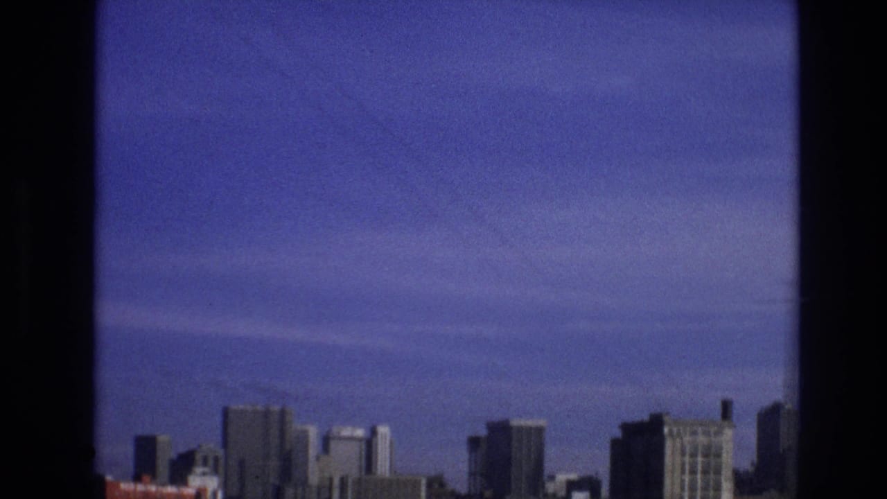 A distant skyline and open sky appear beyond a dark vertical window frame in this purple-tinted 1974 8mm travel view identified as Vail, Colorado.