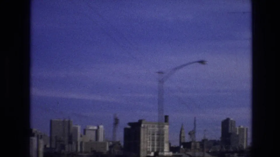 A streetlight, utility lines, and distant buildings appear through the window-framed view in this 1974 8mm clip identified as Vail, Colorado.