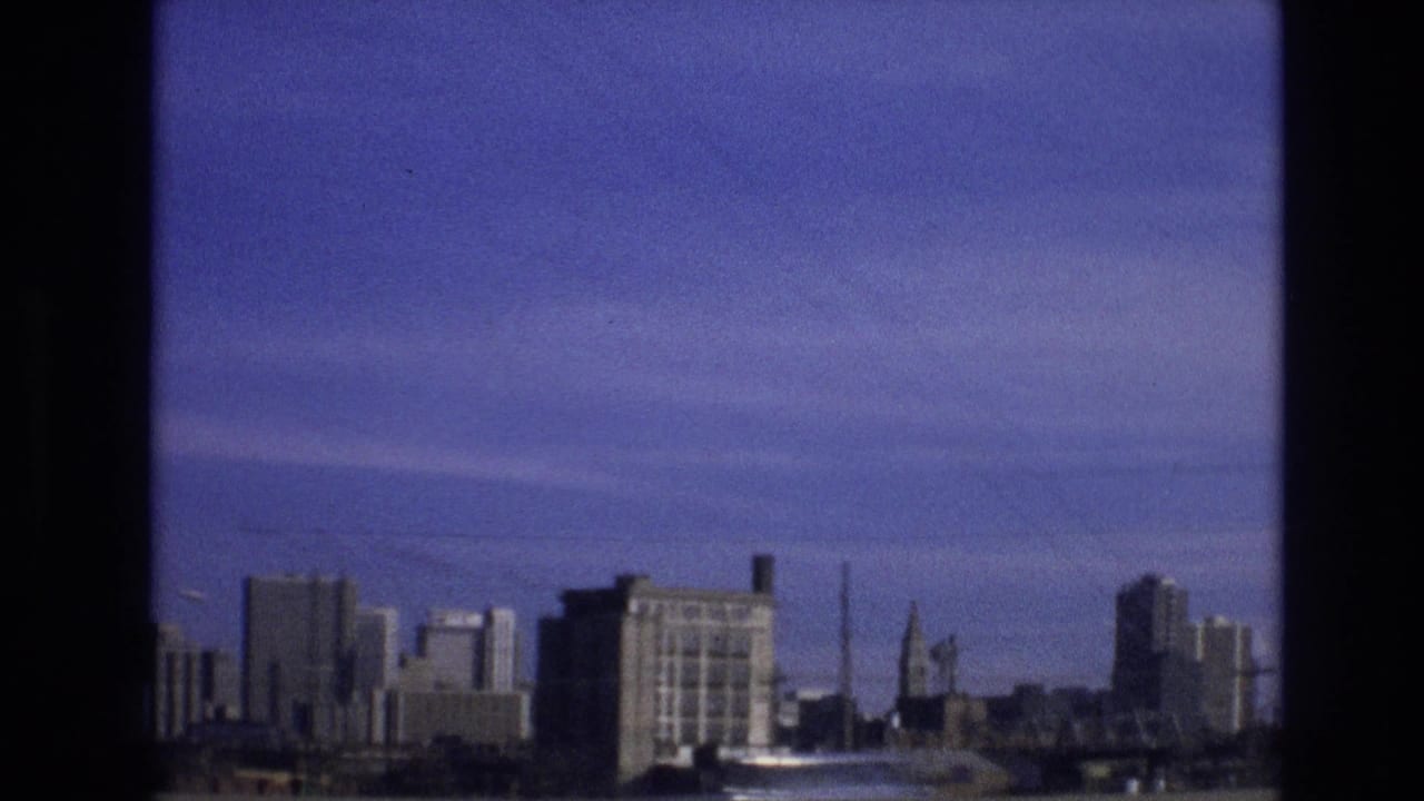 City buildings and a roadside pole seen through dark 8mm frame borders under a blue sky.