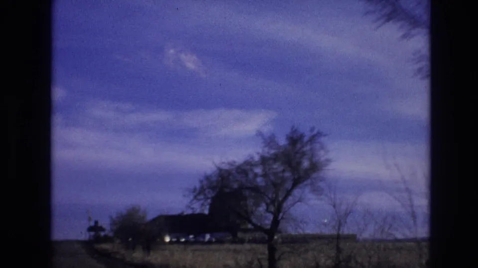 1974 Colorado 8mm frame showing open countryside, bare trees, and a small windmill-like structure beyond a field.