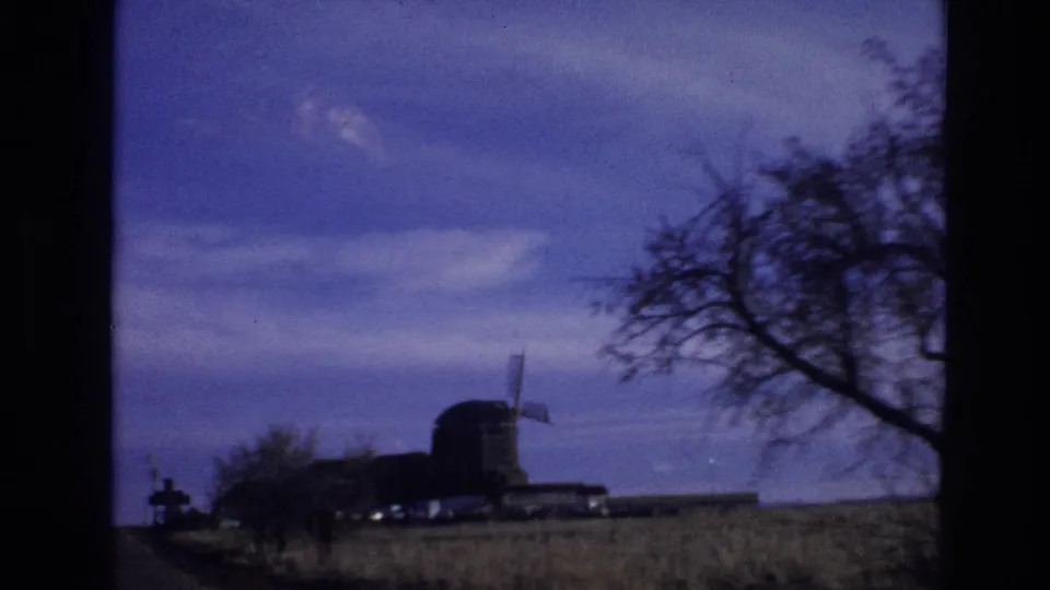 1974 Colorado 8mm travel frame with a bare tree, open field, and small windmill-like structure seen from a moving vehicle.