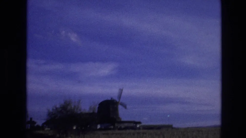 1974 Colorado 8mm frame showing a rural field, low trees, and a small windmill-like structure under a blue sky.