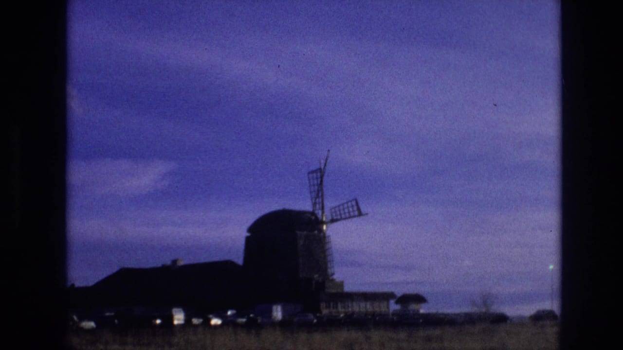 1974 Vail, Colorado frame with a dark windmill silhouette, adjacent low buildings, faint lights near the ground, and open sky viewed from a moving vehicle.