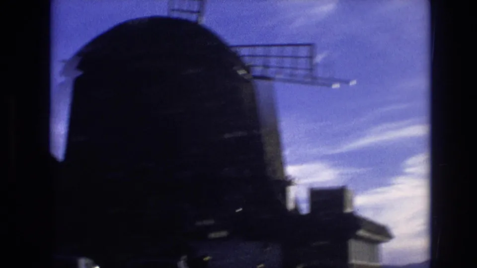 1974 Vail, Colorado 8mm frame showing a dark windmill dome and blade silhouetted against blue sky and pale clouds.