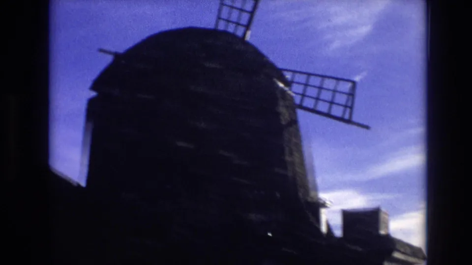 1974 Vail, Colorado home-movie frame with the windmill in heavy silhouette and blade arms extending into a blue, cloud-streaked sky.