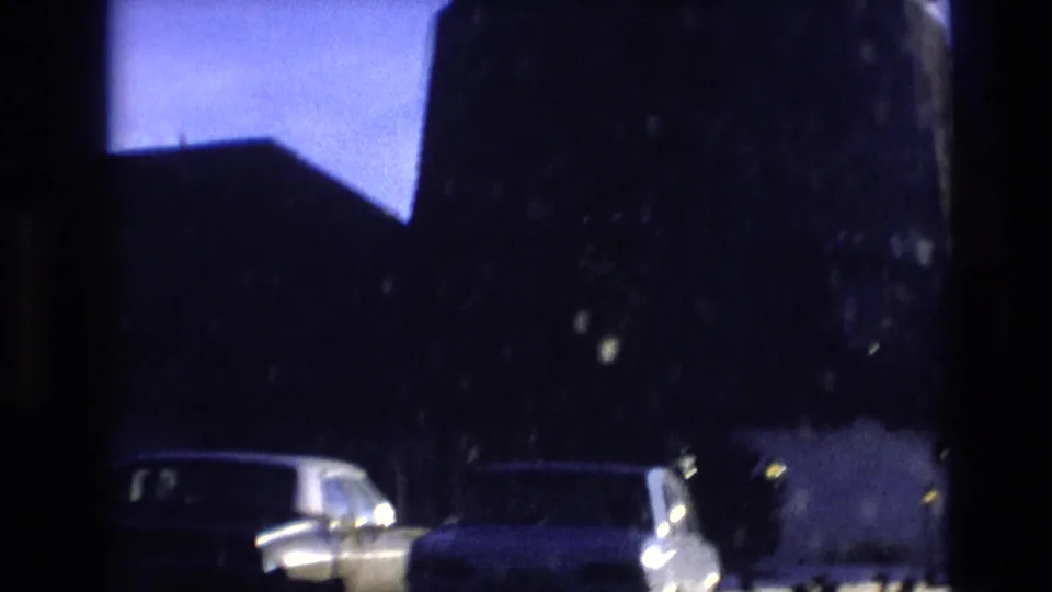 1974 Vail, Colorado frame showing the silhouetted windmill and nearby buildings with two parked cars visible at street level.