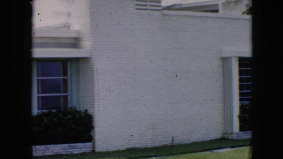 Ground-floor detail of white brick modernist building in Cuba, c.1956, with large horizontal windows and manicured low hedges.