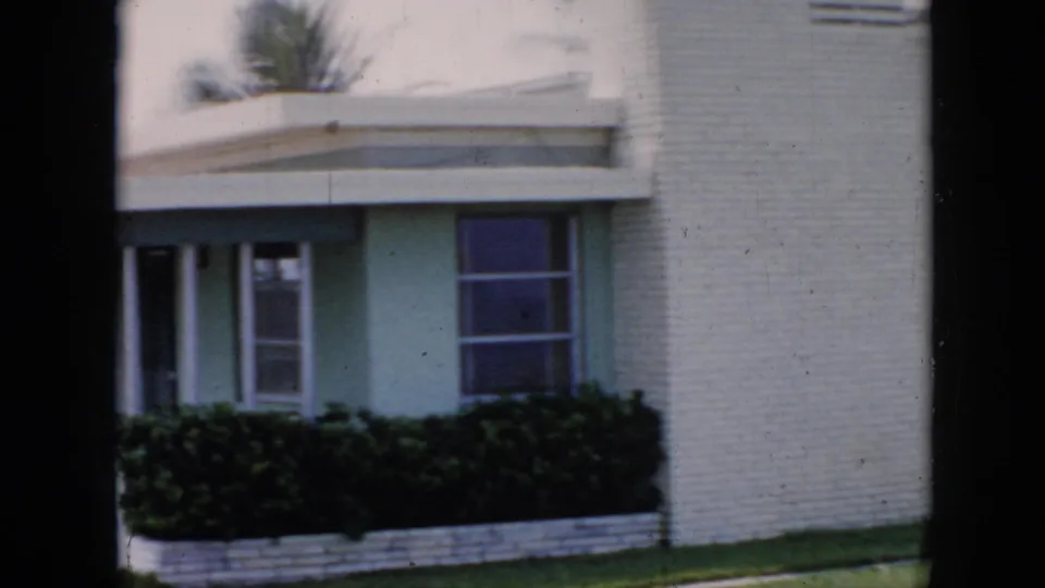 Ground-floor entrance detail of white brick building in Cuba, c.1956, with flat canopy roof, louvered windows, and tropical planting above.