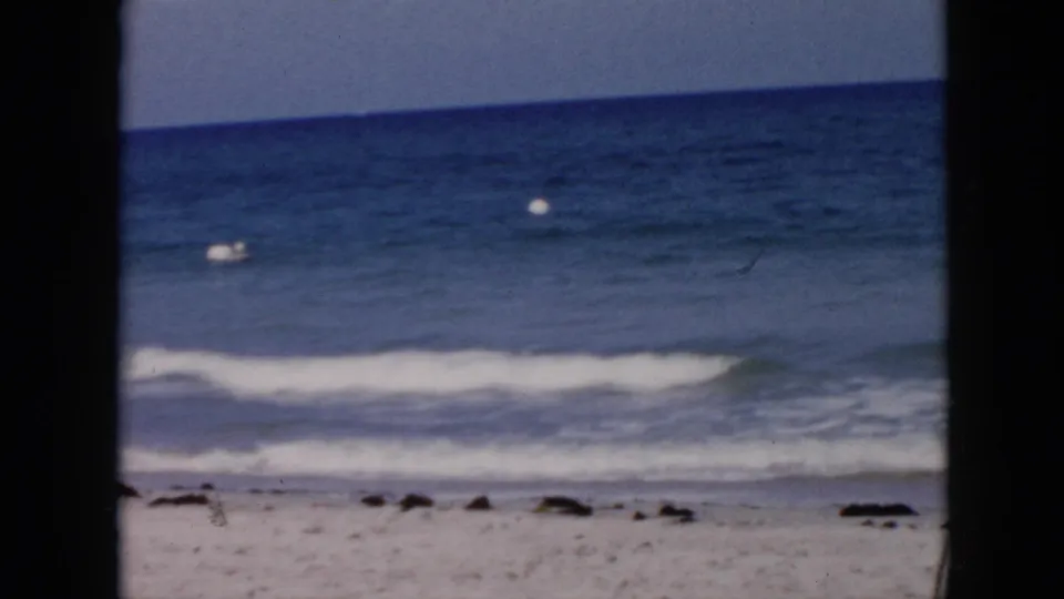 1956 Cuba 8mm frame showing blue ocean, gentle surf, sandy shoreline, and a small white buoy in the distance.