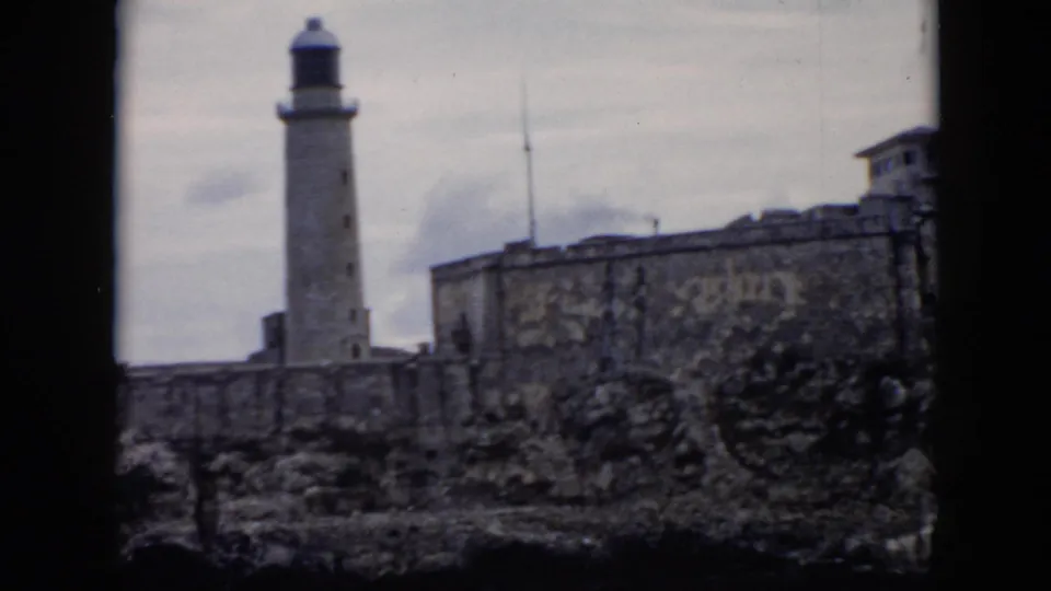 1956 Cuba 8mm frame showing the lighthouse and a large stone wall with a small structure at the edge.