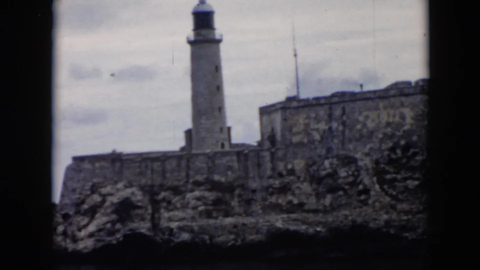 1956 Cuba home-movie frame of the lighthouse, fortification walls, rocks, and overcast sky.