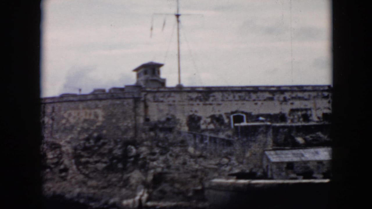 Weathered stone fortress wall with poles and a small structure above it.