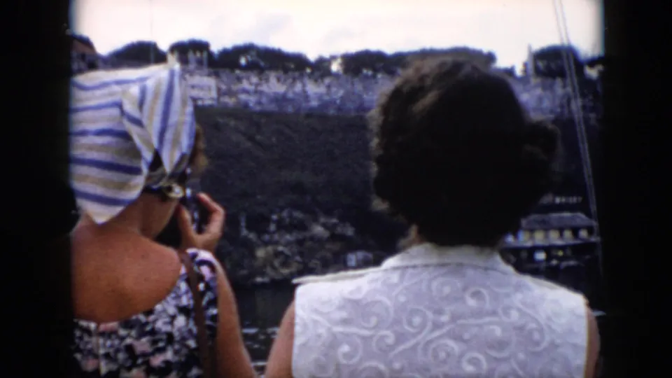 Tourists in 1956 Cuba are filmed from behind while looking toward a historic stone fortress from a sightseeing viewpoint.