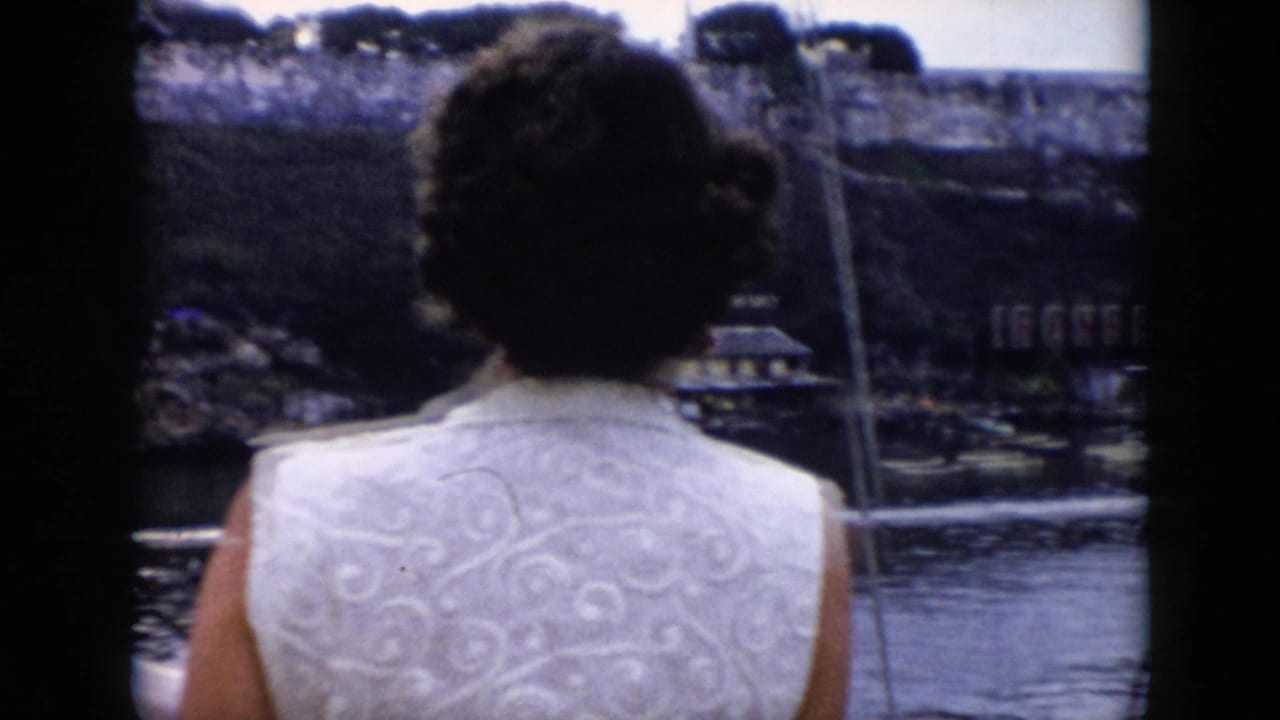 Woman in a white patterned sleeveless top faces a waterfront from a boat.