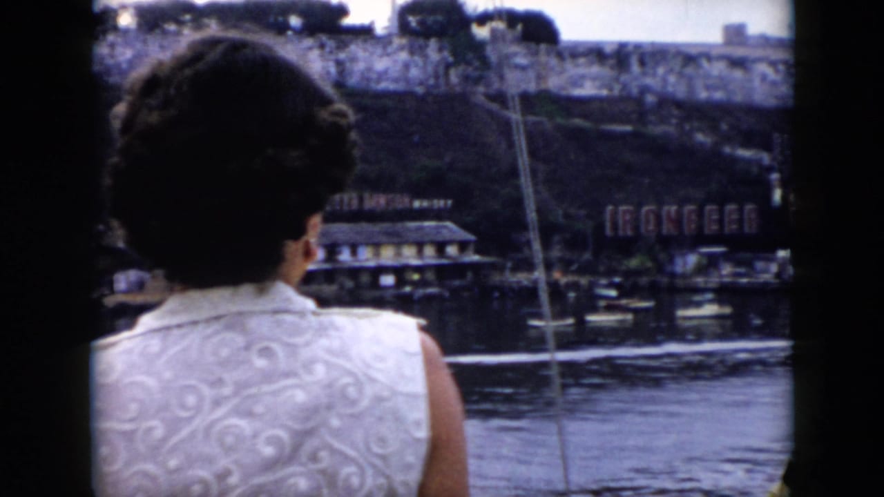 Woman on a boat looks across water toward a riverside sign and shoreline.