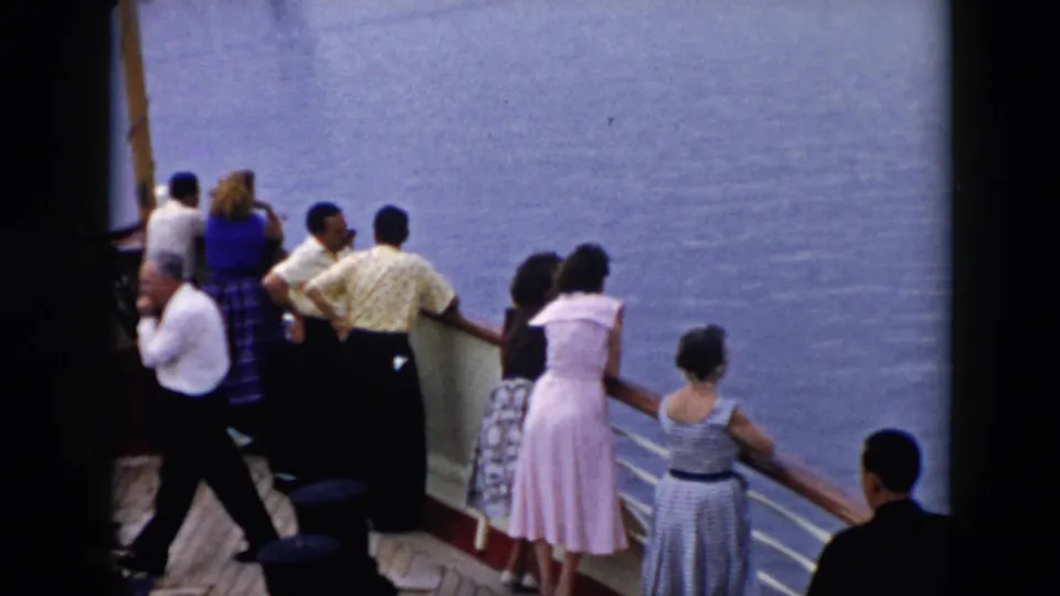 Several passengers in mid-century dress stand at a riverboat railing in Cuba, looking over open water from the deck.