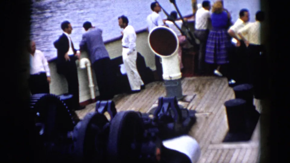 1956 Cuba home-movie frame showing adults on a wooden boat deck, with men at the railing and a large deck vent in the foreground.