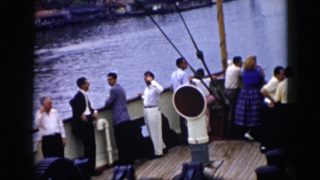 Adults aboard a boat in Cuba, 1956, stand near rigging and a deck vent while looking across the water toward the shoreline.