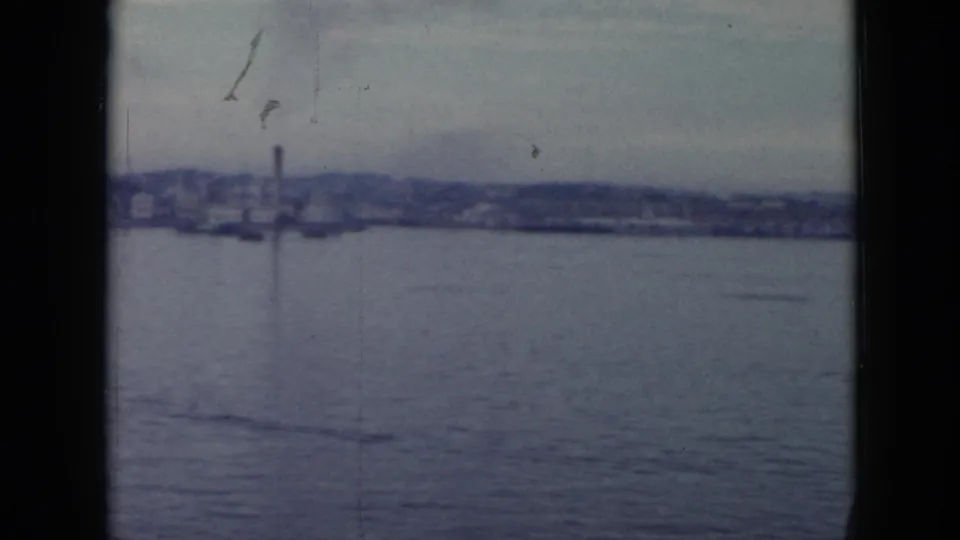 1956 Cuba waterfront view from a boat, with broad water, hazy shoreline buildings, and a vertical smokestack in the distance.