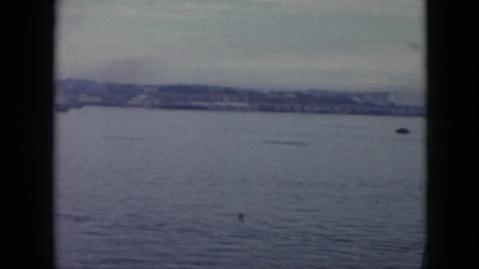 1956 Cuba 8mm frame looking across open harbor water toward a low shoreline, with a small dark vessel-like shape in the distance.