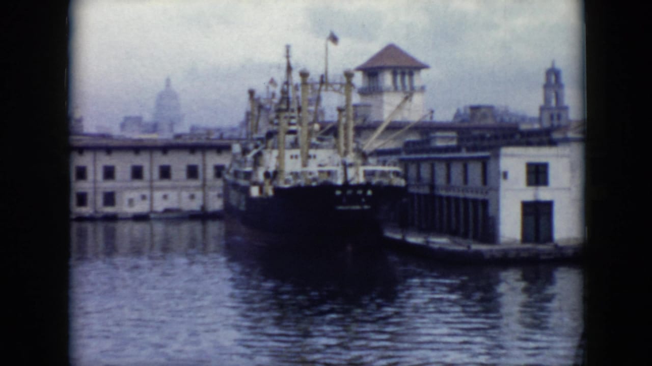 Cargo ship docked beside waterfront buildings with a domed structure in the hazy distance.