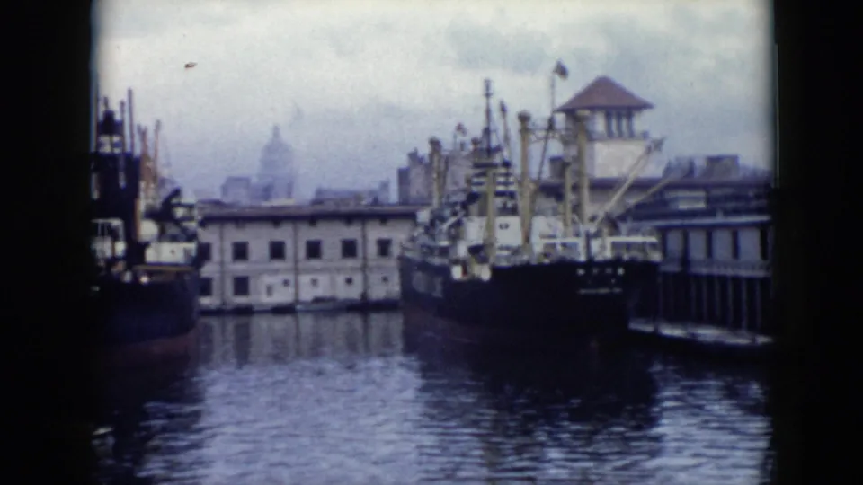 1956 Cuba waterfront scene with a docked cargo vessel, cranes and rigging, low quay buildings, and a distant domed skyline element.