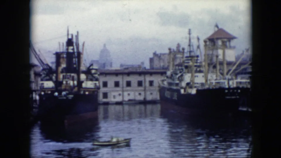 1956 Cuba harbor footage showing docked cargo vessels, cranes, quay buildings, and a small boat moving across the foreground water.