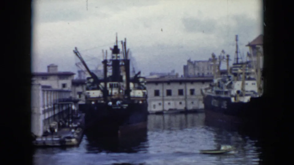 1956 Cuba port view with large vessels along the quay, industrial dock structures, low waterfront buildings, and a small boat on calm water.