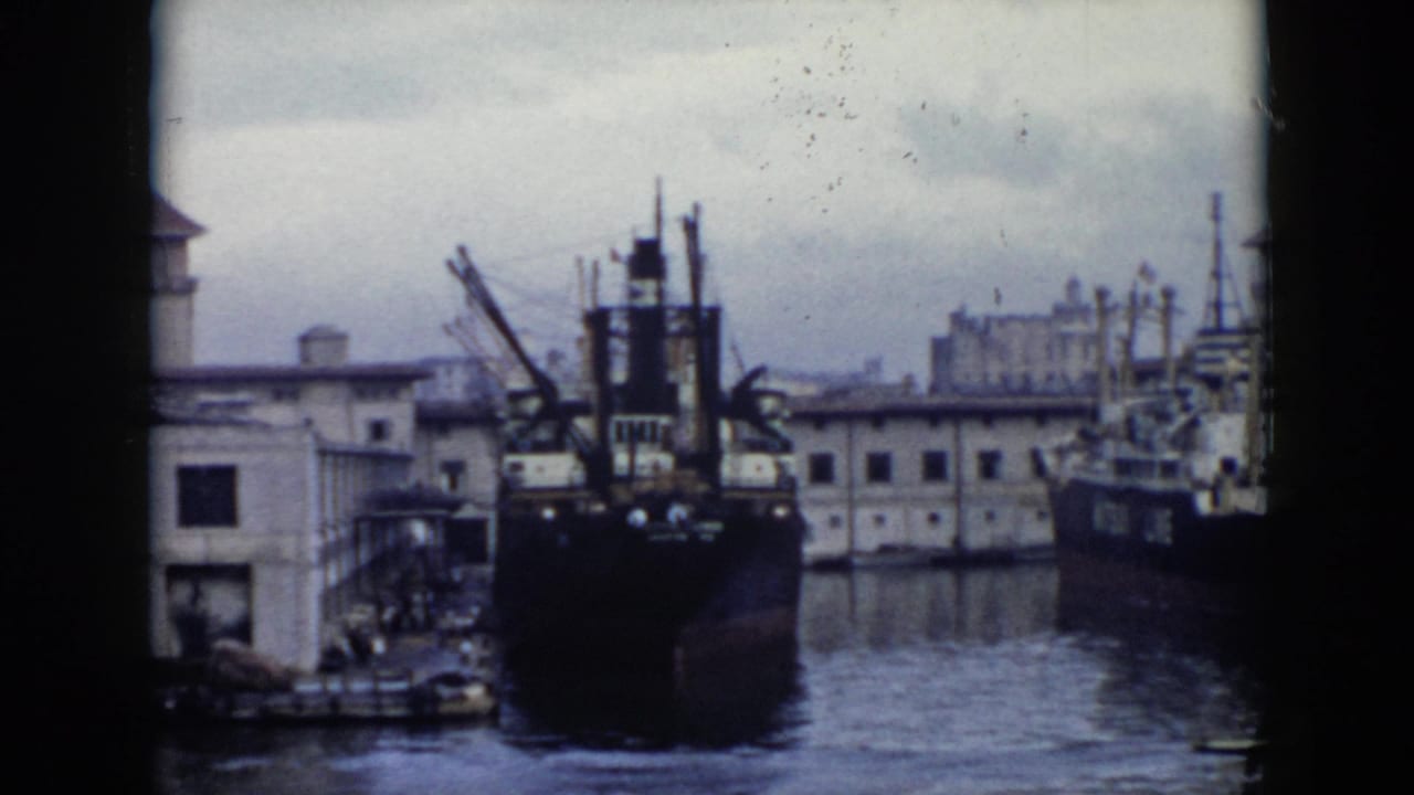1956 Cuba harbor view with large docked ships, cranes, waterfront buildings, and calm water in soft 8mm color.