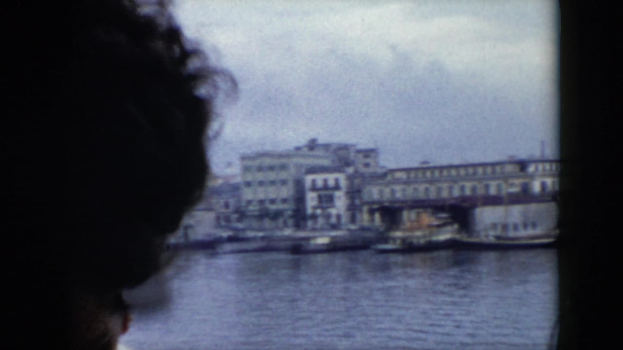 1956 Cuba home-movie frame showing a dark passenger silhouette inside a ferry and a waterfront view through the window.