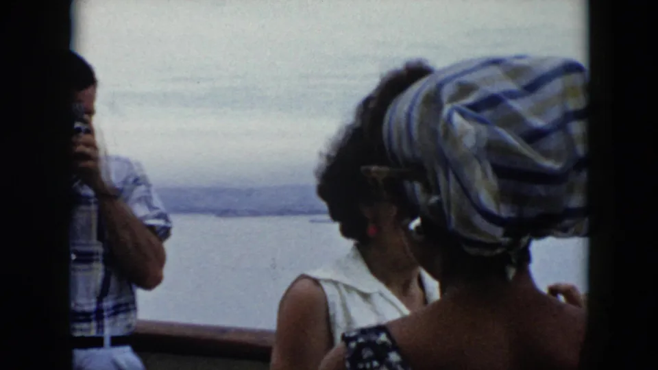 1956 Cuba home-movie frame of ferry passengers, including women near the window and a partly seen man using a camera.