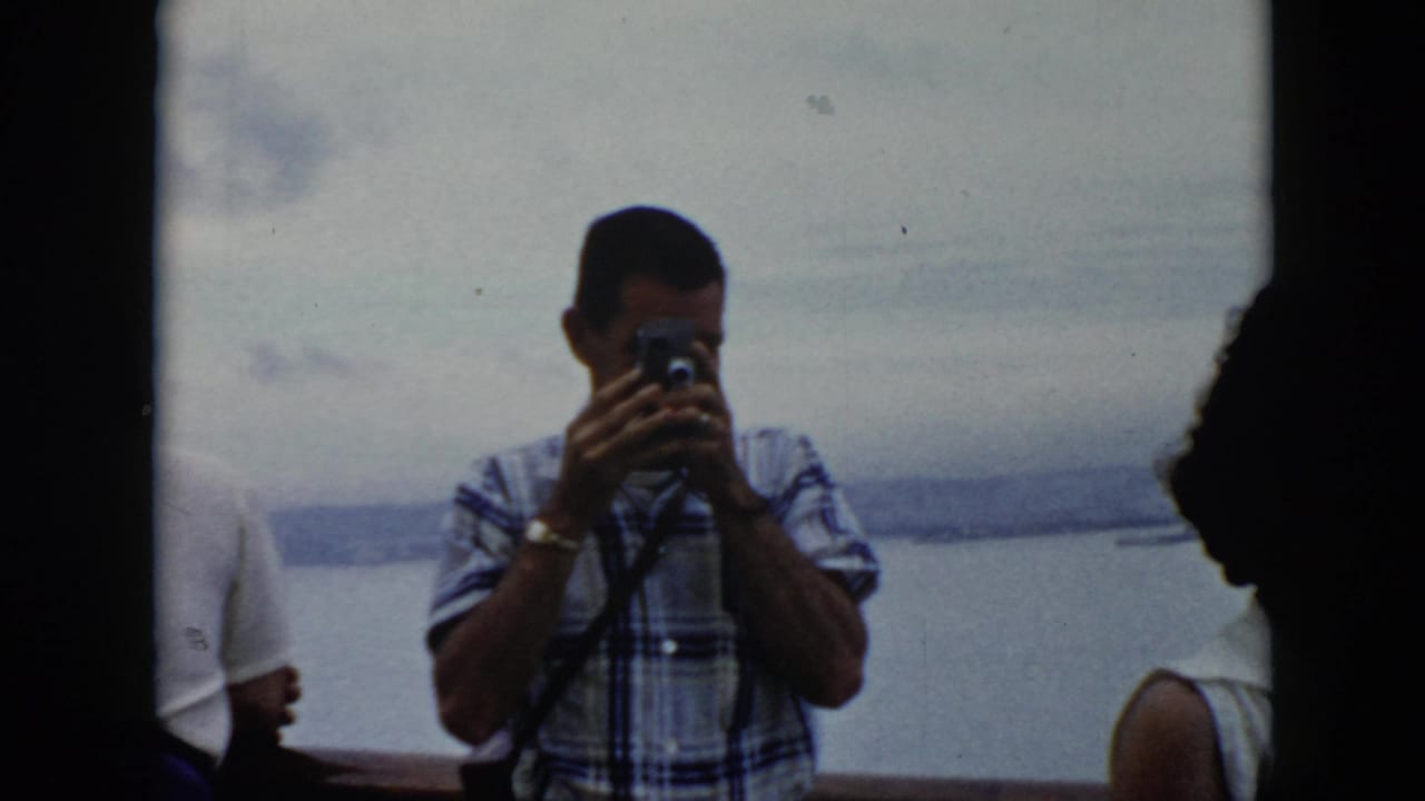 In Cuba 1956 home-movie footage, a man in a plaid shirt photographs from a boat beside other passengers.