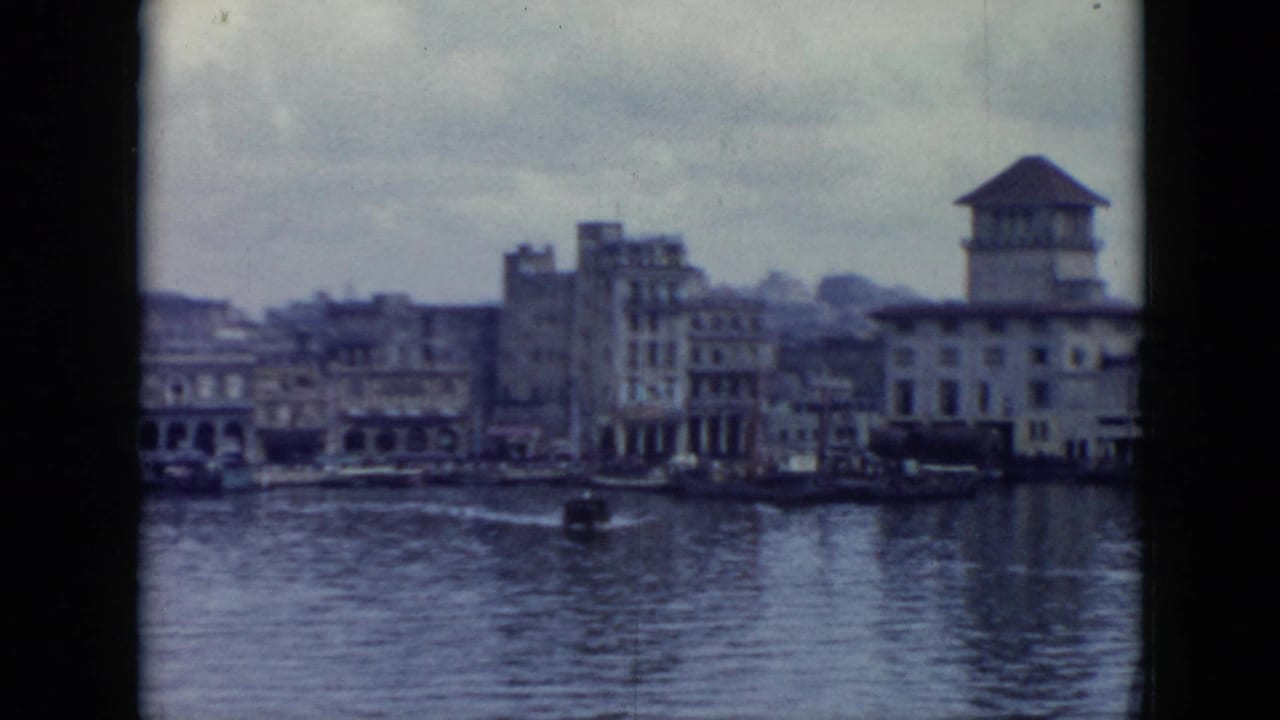 Cuba 1956 waterfront view from a boat, with multi-story buildings, a tower, water, and overcast sky.