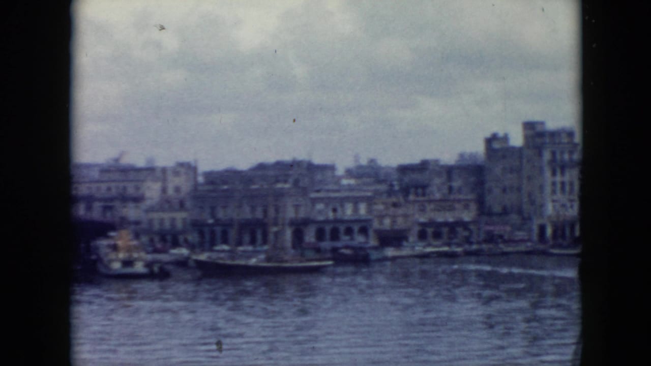 1956 Cuba waterfront view with arched buildings, docked boats, rippled harbor water, and soft 8mm color fading.