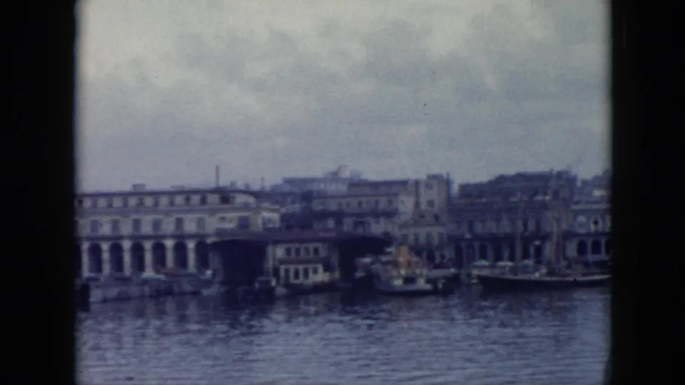 1956 Cuba waterfront view with a long arched building, small boats, and hazy harbor reflections on 8mm film.
