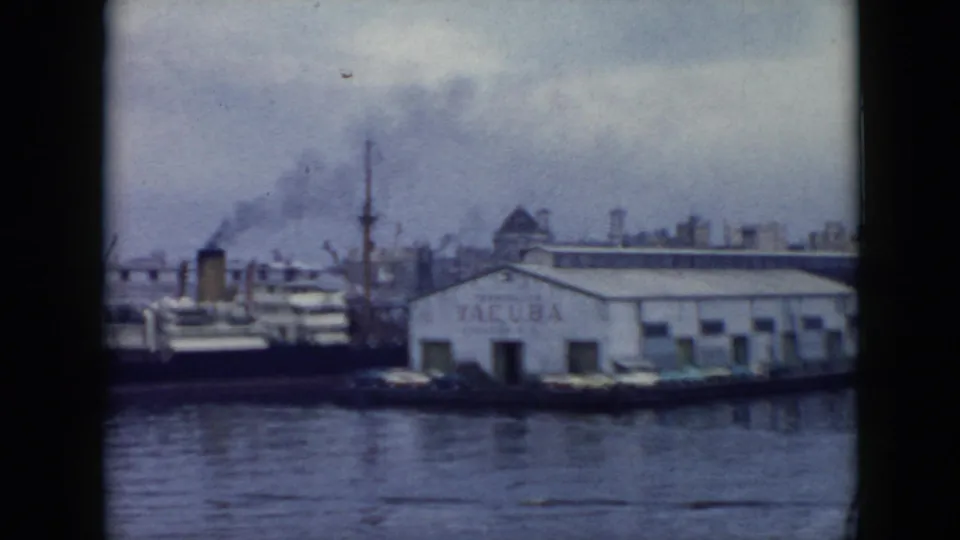 1956 Cuba waterfront with a white VACUBA warehouse, docked ships, smokestack smoke, cranes, and muted harbor reflections.