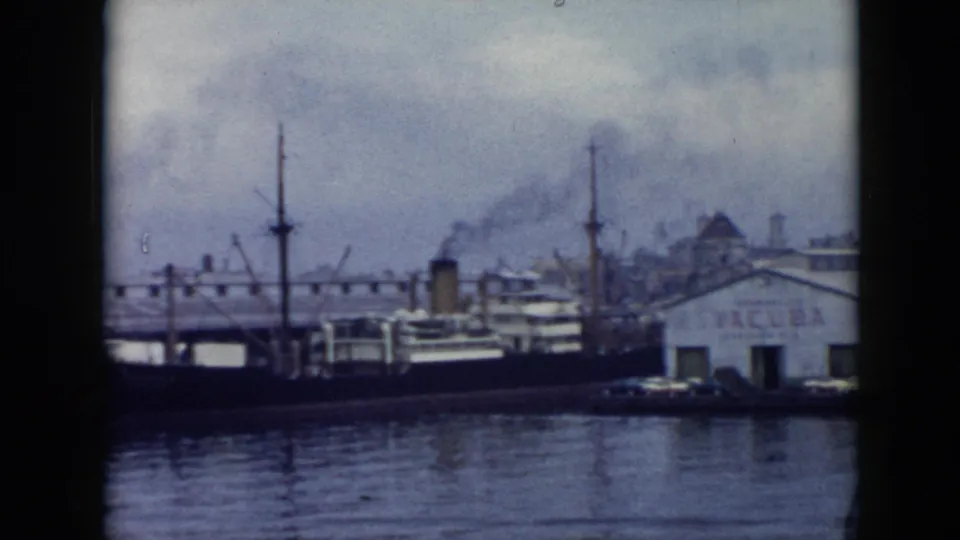 1956 Cuba waterfront view with docked boats, crane masts, smoke over industrial buildings, and the edge of a VACUBA warehouse.