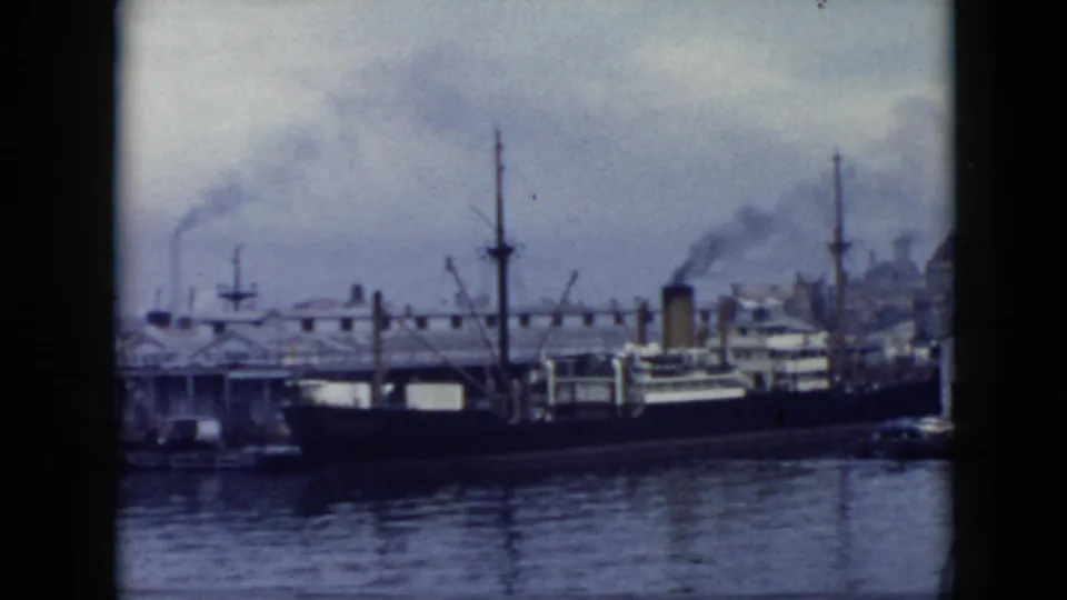 1956 Cuba harbor view of a moored dark-hulled transport ship, cranes or masts, dock buildings, and industrial smoke behind the waterfront.