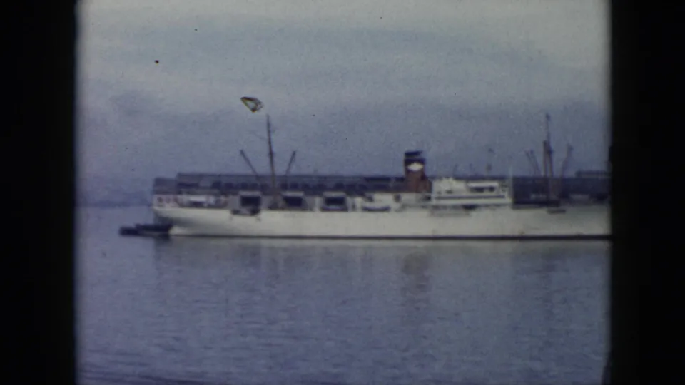 1956 Cuba harbor view showing a white moored ship, calm water, cranes, dock buildings, and a hazy industrial backdrop.